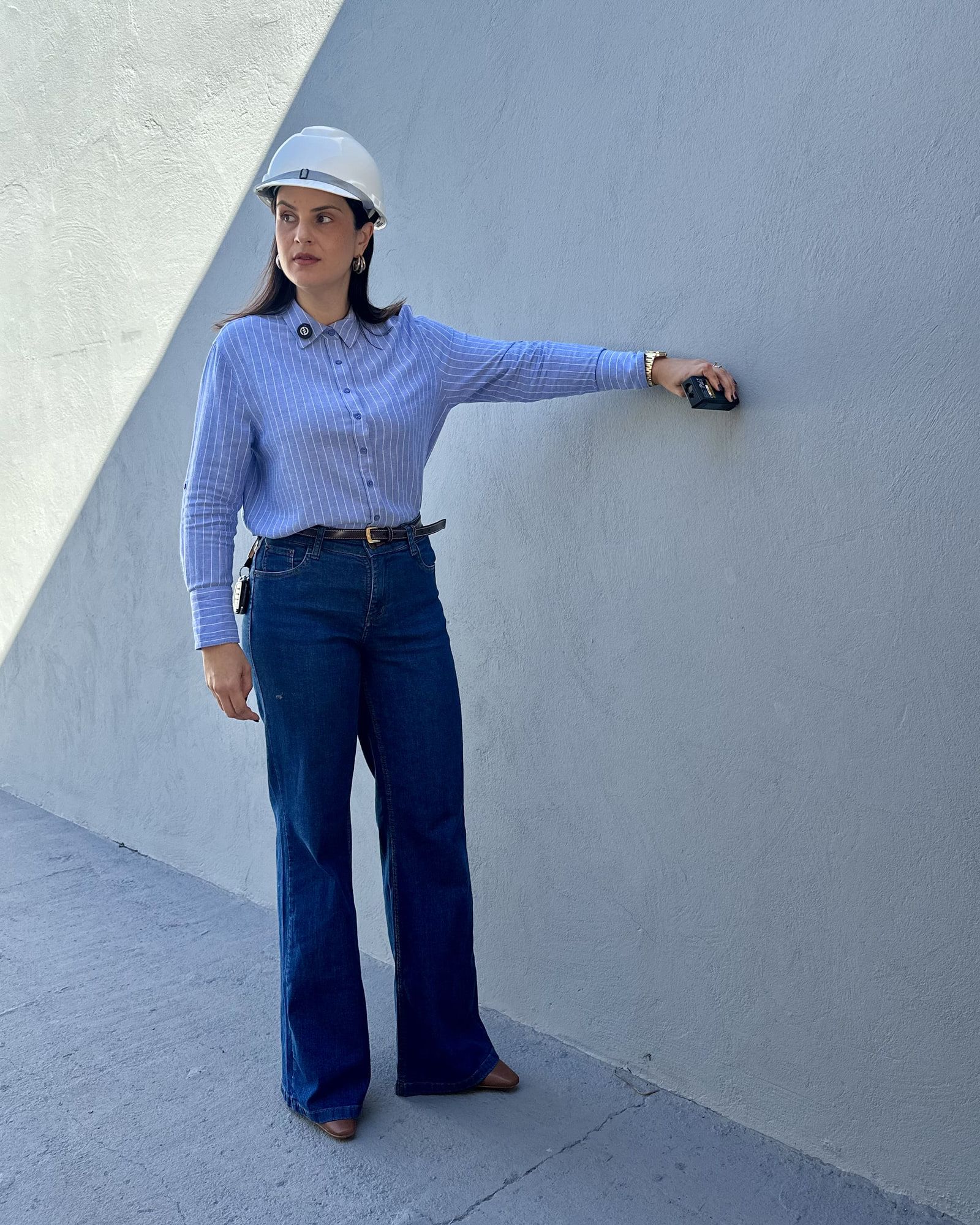 Viviane Bermal em vistoria técnica, de capacete, apoiando instrumento de medição na parede de uma edificação.