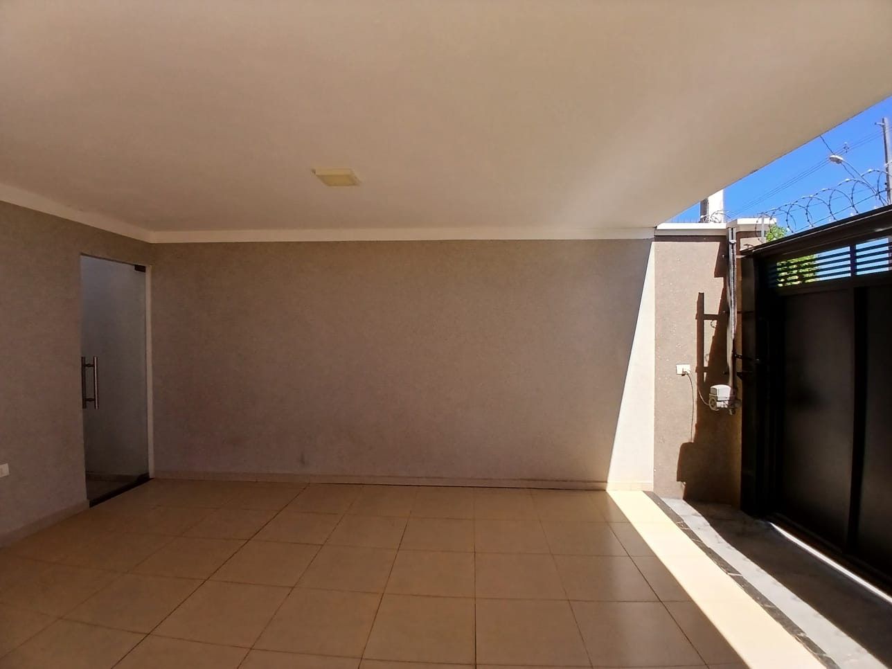 Ambiente interno vazio de imóvel, com piso cerâmico, esquadria e acesso para a rua.