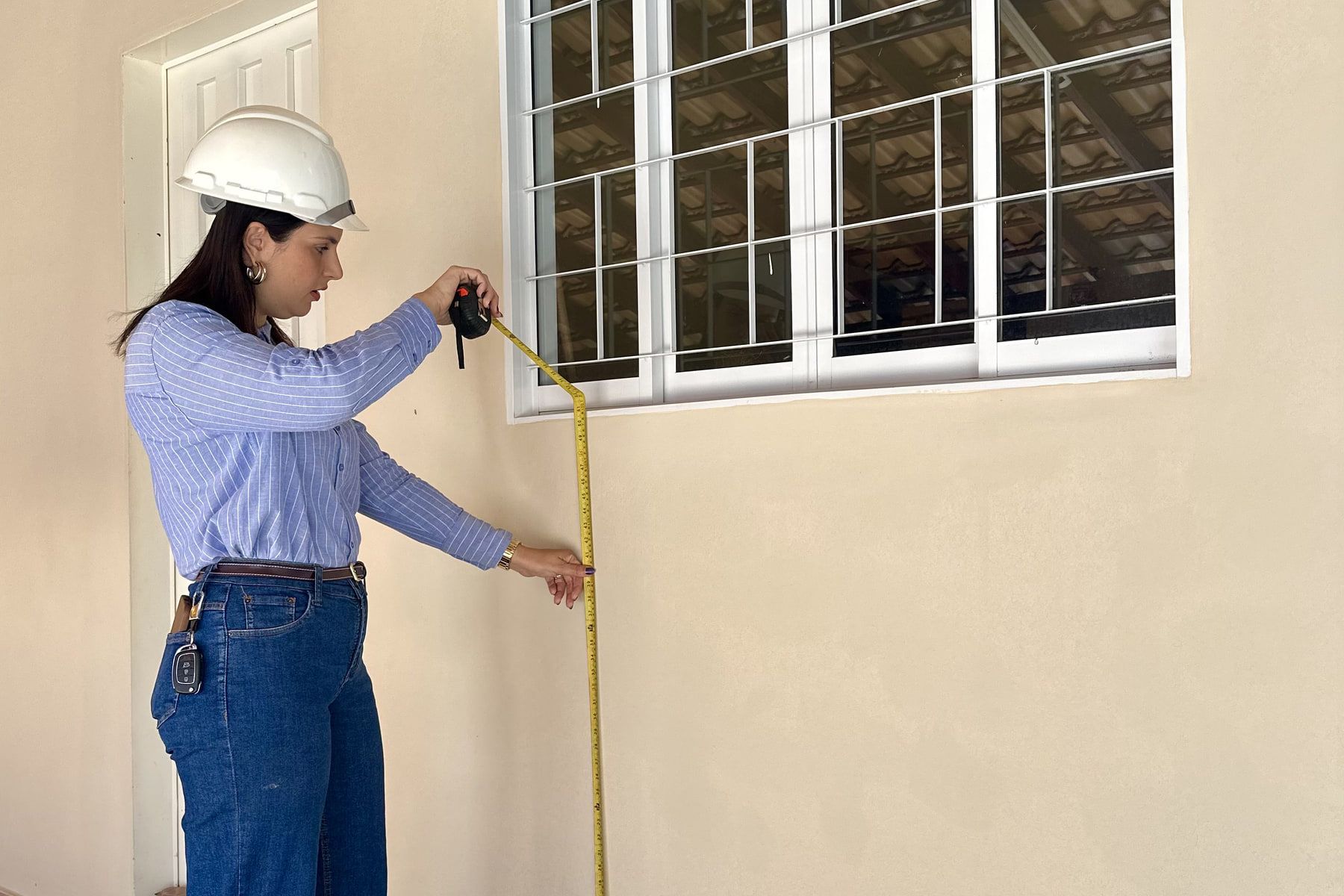 Viviane Bermal medindo o vão de uma janela com trena, durante vistoria técnica.